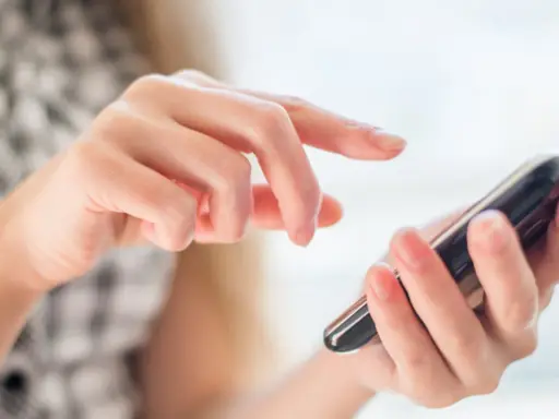 Dłoń trzymająca smartfon, palec wskazujący dotyka ekranu.