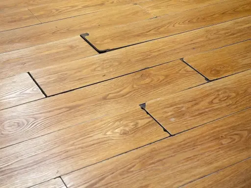 Suelo de madera con tablas levantadas y espacios oscuros, indicando posible daño por humedad. Se busca cómo quitar mancha negra humedad madera.