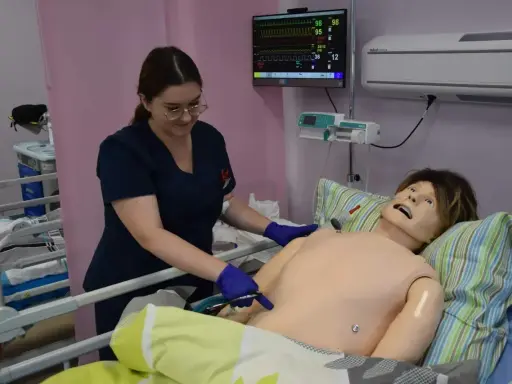 Studentka stomatologii ćwiczy procedury medyczne na fantomie. Monitor parametrów życiowych pokazuje dane.