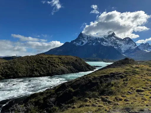 Wodospad w **Torres del Paine** z turkusową wodą i ośnieżonymi szczytami w tle.