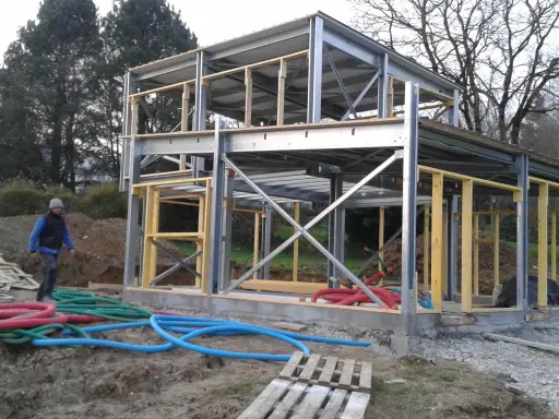 Chantier d'une maison ossature métallique. Le prix est un facteur clé pour ce type de construction moderne. Des tuyaux colorés sont visibles au sol.