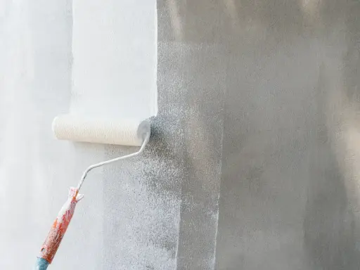Rodillo blanco aplica pintura a pared gris. Se ve el proceso de cuantas manos de pintura se le da a una pared para un acabado perfecto.
