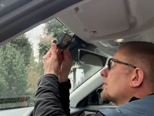 Mężczyzna montuje kamerę samochodową nad lusterkiem wstecznym. Dbałość o szczegóły podczas instalacji zapewnia bezpieczeństwo na drodze.