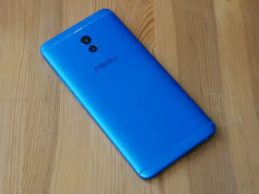 Niebieski smartfon Meizu M6 Note z podwójnym aparatem z tyłu leży na drewnianym blacie.