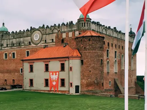 Majestatyczny zamek golubski z polską flagą i innymi flagami narodowymi na trawiastym dziedzińcu.