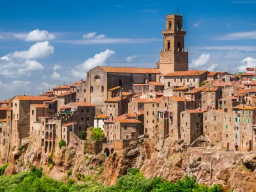 Eine malerische Stadt in der Toskana thront auf einem Felsen, umgeben von grünen Hügeln und blauem Himmel mit Wolken.