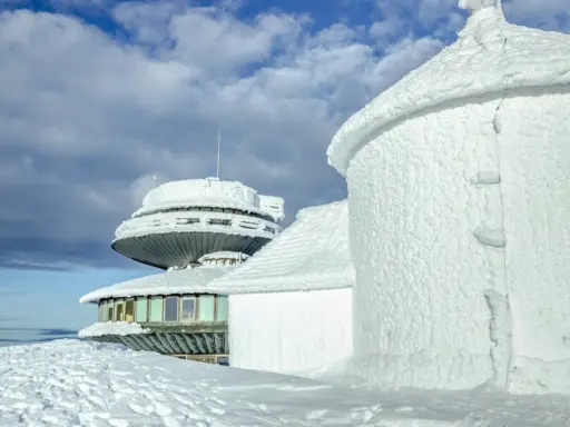 Zimowe krajobrazy na Śnieżce. Budynki obserwatorium pokryte lodem i śniegiem, niebo z chmurami.