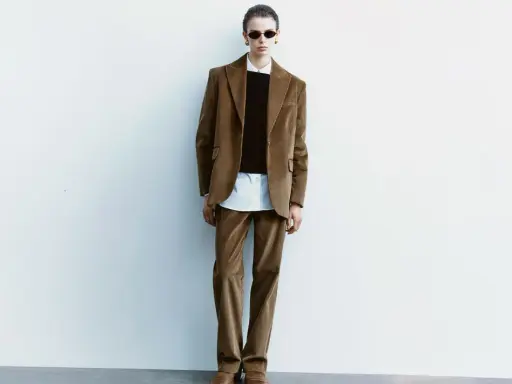 Model in a brown corduroy suit, white shirt, and black sweater, wearing sunglasses.