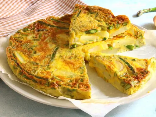 Una gustosa frittata di asparagi, con patate e uova dorate, tagliata a fette su un piatto bianco.