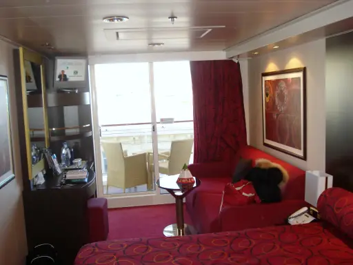 Cabina su MSC Divina, ponte 9, con balcone, divano rosso, letto e quadro astratto.