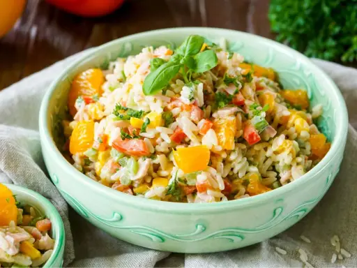 Erfrischender Reissalat mit Mandarinen, Paprika und Kräutern, garniert mit Basilikum.