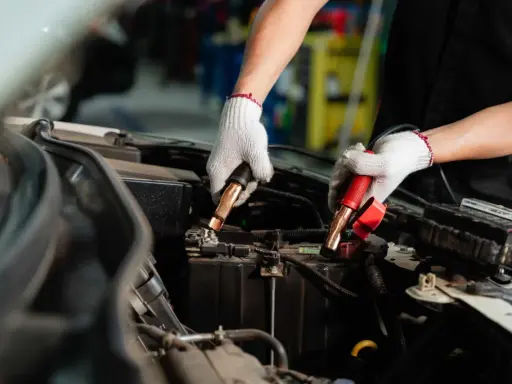 Manos enguantadas conectando cables a la batería del coche. Es hora de desconectar la batería del coche para un mantenimiento seguro.