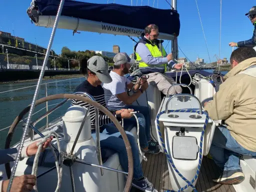 Apprentissage d'un nœud marin sur un voilier. Plusieurs personnes s'exercent à faire des nœuds avec des cordages blancs et bleus.