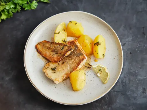 Gebratener Seehecht mit Haut, serviert mit Salzkartoffeln und Zitrone. Ein köstliches Gericht, das zeigt, wie man Seehecht mit Haut zubereitet.