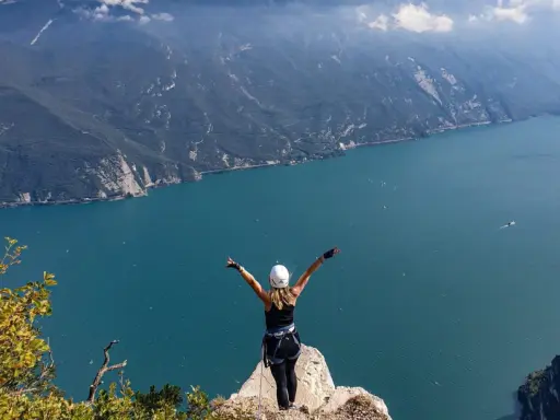 Kobieta z rękami w górze na szczycie klifu, podziwiająca jezioro Garda po przejściu via ferrata.