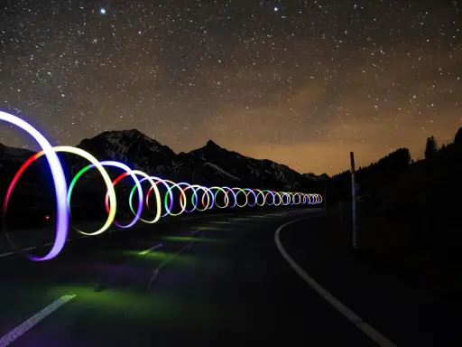 Una carretera nocturna bajo un cielo estrellado, con aros de luz de colores que parecen flotar. ¡Trucos fotos geniales!