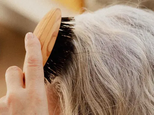 Une main brosse des cheveux gris, secs, peut-être liés à la ménopause, avec une brosse en bois.
