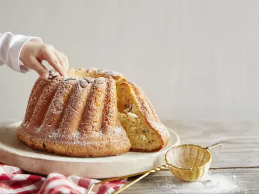 Un enfant touche un Kougelhopf, une des spécialités alsace, saupoudré de sucre glace. Une tranche est coupée, révélant des raisins secs.
