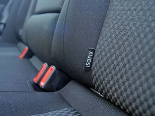 Etiqueta negra con el **símbolo ISOFIX** en el asiento de un coche, junto a los anclajes de seguridad.