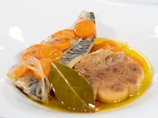 Deliciosa caballa en escabeche con zanahorias, cebolla y laurel en un plato blanco.