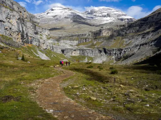 Wanderer auf einem Pfad im Ordesa Nationalpark, umgeben von steilen Felswänden und schneebedeckten Gipfeln.