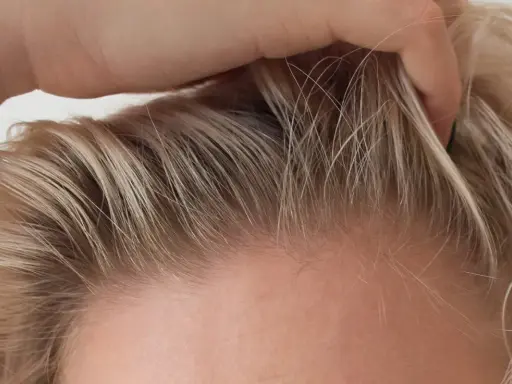 Dłoń delikatnie przeczesuje jasne włosy, ukazując drobne kosmyki, które zdradzają, jak ujarzmić baby hair.