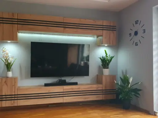 Nowoczesne meble do małego mieszkania: wisząca szafka RTV z podświetleniem, kwiaty i duży zegar na ścianie.