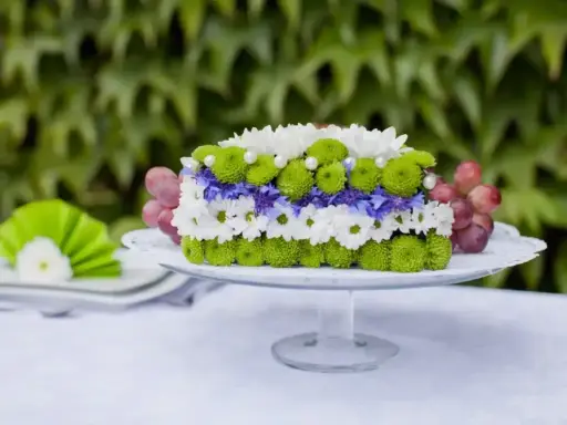 Inspiracja na bukiety na stół weselny: kwiatowy tort z chryzantem, chabrów i winogron na paterze.