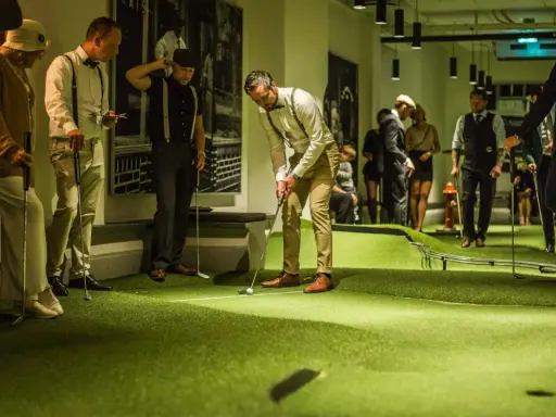 Människor i festliga kläder spelar minigolf på Golfbaren Stockholm.
