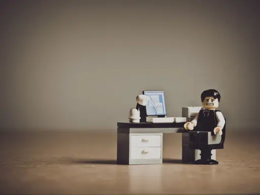 Figurka Lego przedstawiająca zestresowanego pracownika siedzącego przy biurku z komputerem.
