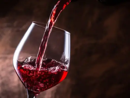 Vino tinto se vierte en una copa, creando burbujas y espuma. Un brindis por el día del vino.