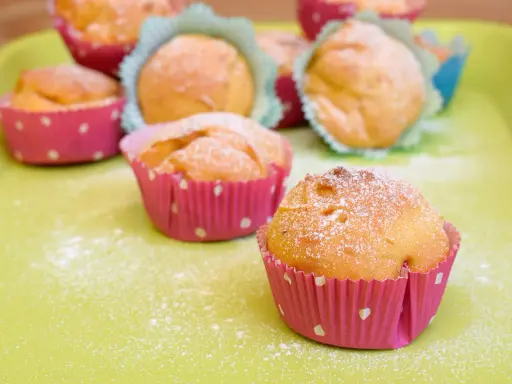 Leckere Muffins ohne Ei, bestäubt mit Puderzucker, in bunten Papierförmchen auf hellgrüner Unterlage.