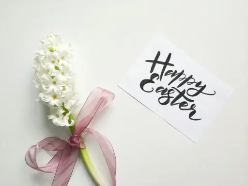 Un giacinto bianco legato con un nastro rosa, accanto a un biglietto con scritto "Happy Easter". Come una poesia campane di Pasqua di Gianni Rodari.