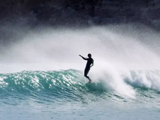Surfer in Aktion auf einer Welle an der Algarve. Die Gischt spritzt, während er die portugiesische Küste genießt.