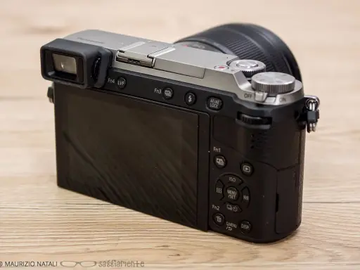 Retro della fotocamera Panasonic Lumix GX80 con obiettivo. Schermo LCD e mirino elettronico visibili.