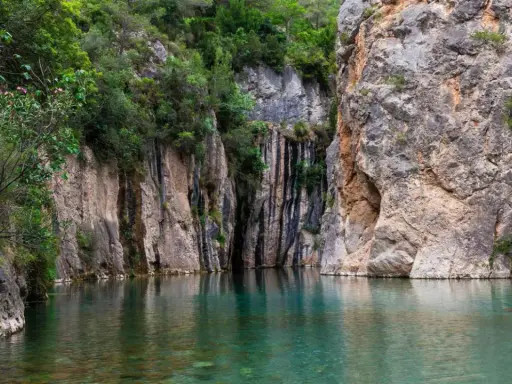 Aguas cristalinas reflejan imponentes rocas y vegetación exuberante en estas piscinas naturales de Castellón. Un rincón idílico para refrescarse.