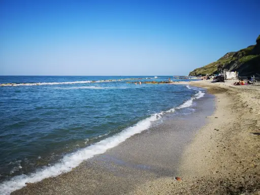 La **spiaggia** di **Castel di Mezzo** baciata dal sole, con il mare azzurro e la collina verde sullo sfondo.