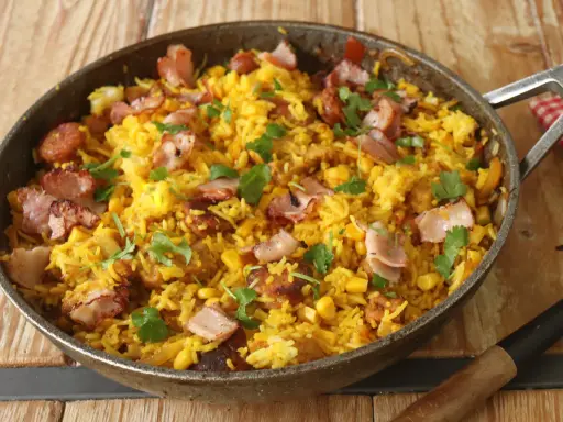 Arroz paisa en sartén, con trozos de tocino crujiente, maíz y cilantro fresco. ¡Un festín para los sentidos!