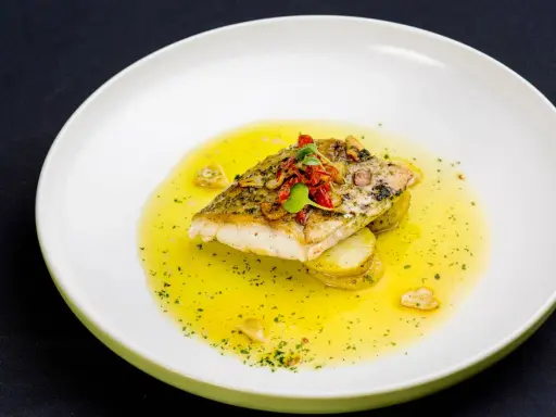 Filet ryby w aromatycznym sosie cytrynowym, podany na plastrach ziemniaków.