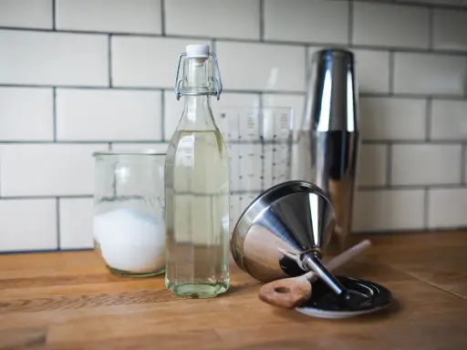 Zutaten für zuckersirup selber machen: Zucker in einem Glas, Sirup in einer Flasche, Cocktail-Shaker und Trichter.