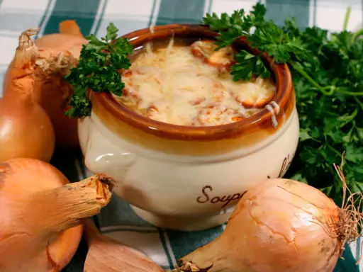 Un bol de soupe à l'oignon gratinée, un plat parisien réconfortant, entouré d'oignons frais et de persil.