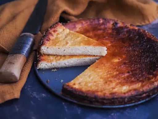 Un fiadone corse, un gâteau au fromage et au citron, est servi avec une tranche coupée, à côté d'un couteau sur un tissu ocre.