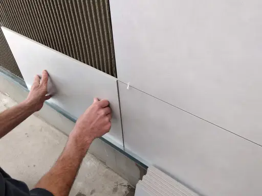 Ręce układają płytki 30x60 na ścianie, tworząc równą, nowoczesną powierzchnię. Widać klej i krzyżyki dystansowe.
