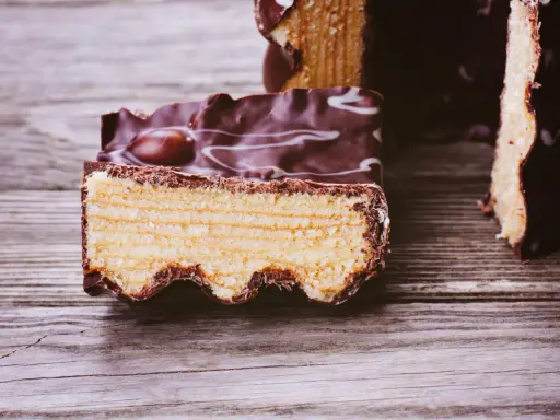 Ein Stück Baumkuchen mit Schokoladenglasur und weißen Zuckerguss-Wirbeln, perfekt für ein Baumkuchen Rezept.