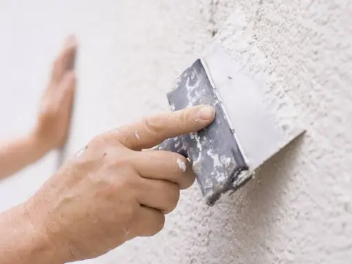 Mano aplicando masa con espátula para reparar gotele en pared.