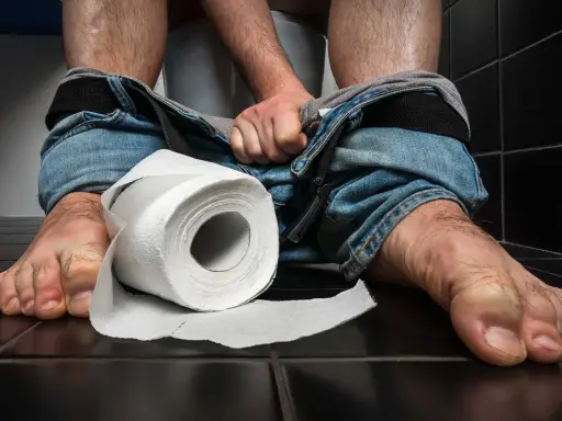 En person sitter på en toalett med neddragna jeans. En rulle toalettpapper ligger bredvid. Tänk på vaccin mot turistdiarré för en tryggare resa.