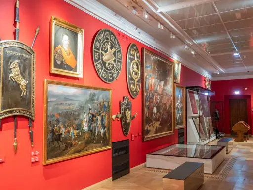 Wnętrze jednego z muzeów w Krakowie. Czerwone ściany zdobią obrazy batalistyczne, portrety i historyczne tarcze.