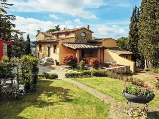 Un perfetto weekend in Toscana: villa con giardino fiorito, cipressi e un cielo azzurro con nuvole bianche.