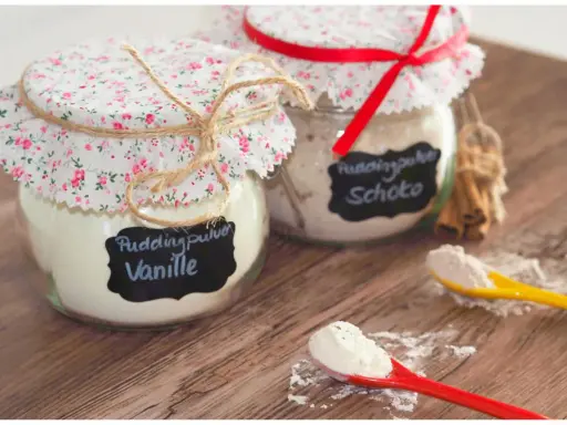Zwei Gläser mit selbstgemachtem Puddingpulver (Vanille & Schoko) auf einem Holztisch, bereit für köstliche Desserts.