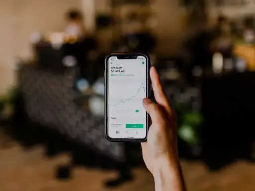 Mano sosteniendo un teléfono que muestra el gráfico de acciones de Amazon, una opción para saber donde invertir dinero.